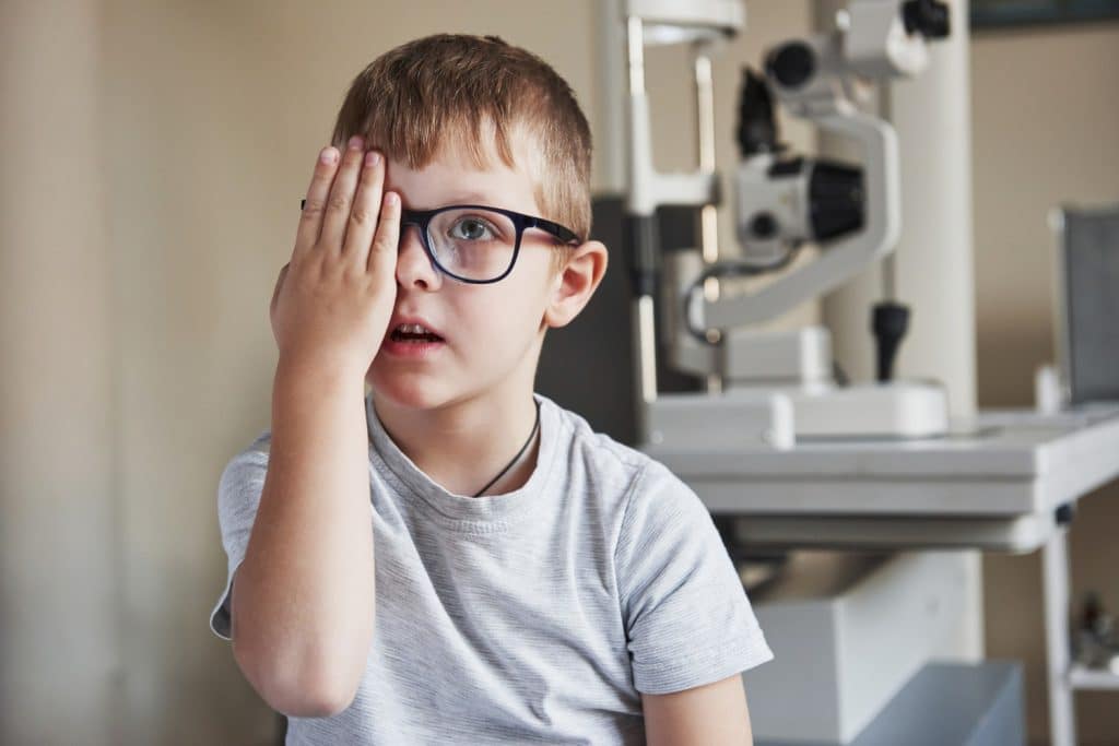 Niño con gafas tapándose un ojo durante una consulta oftalmológica