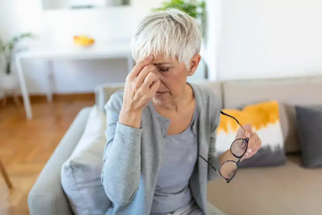 Mujer sentada con dolor de cabeza, sujetando unas gafas